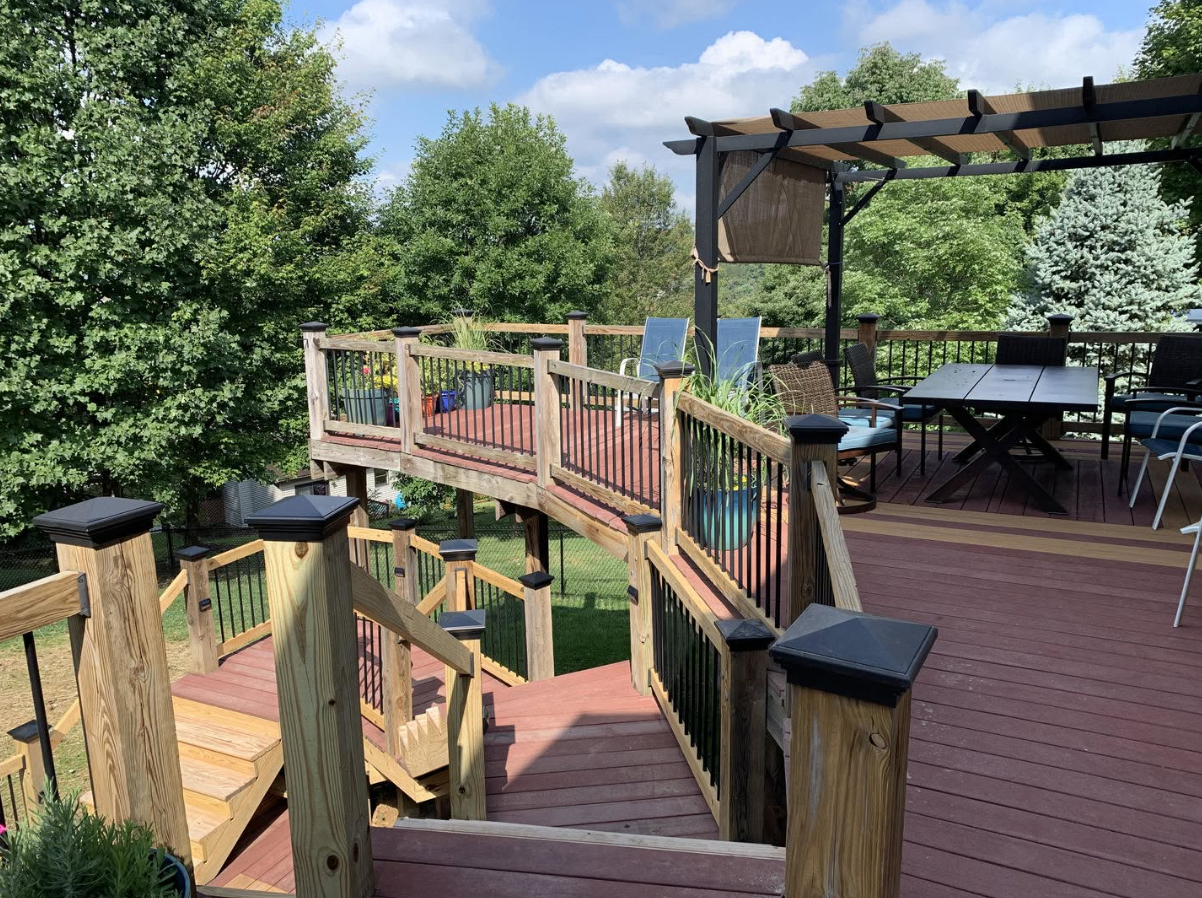 A wide view of an outdoor wooden deck, featuring a common area with a table and chairs, as well as stairs leading down. A wide view of an outdoor wooden deck, featuring a common area with a table and chairs, as well as stairs leading down.