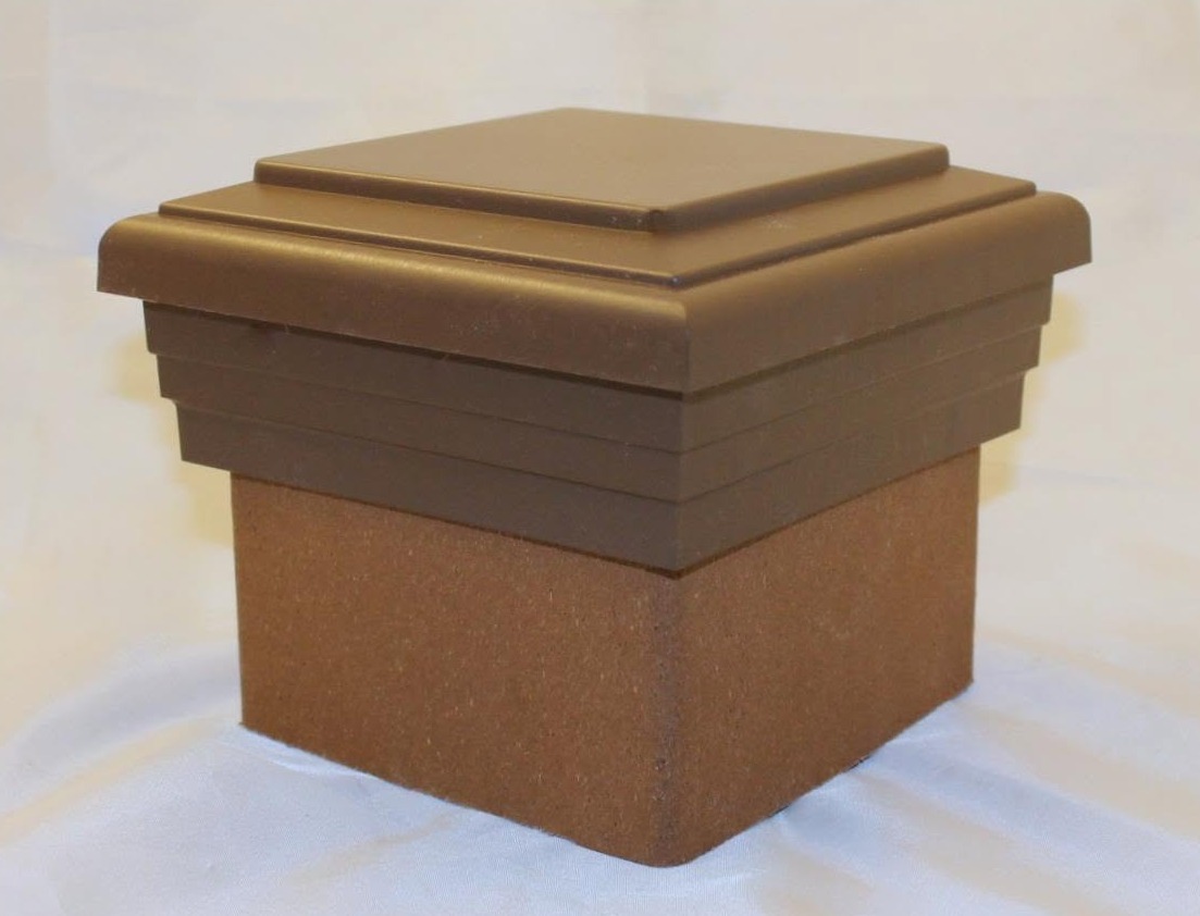A close-up of a brown square post cap with layered edges resting on a white cloth against a plain background.