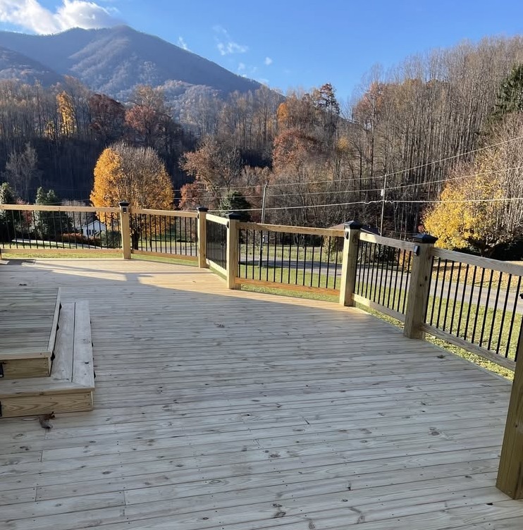 A wide wooden deck with railings overlooking a road, autumn trees, and mountains under a clear blue sky.