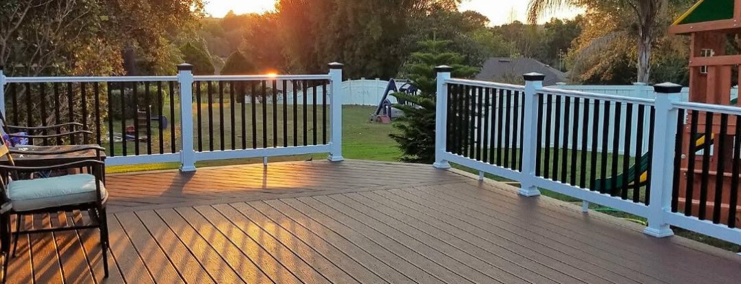 How To Measure Your Deck or Fence for Post Caps A wide deck with white-and-black railings, outdoor chairs, a grassy yard, and sunset light in the distance.