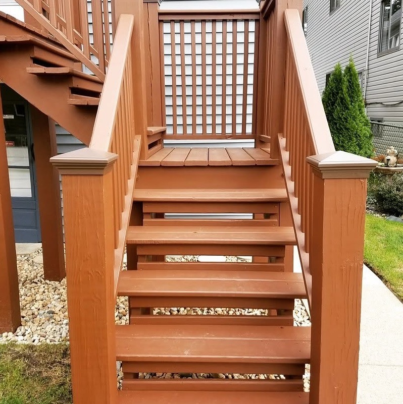 A brown deck staircase with matching railings, square posts, and lattice panels between neighboring houses.