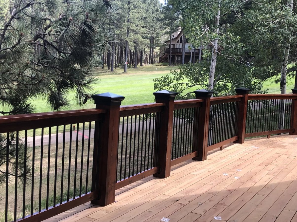 What Are the Benefits of HDPE for Post Caps? A wood deck with black metal railing panels and post caps overlooking trees, grass, and a nearby house.